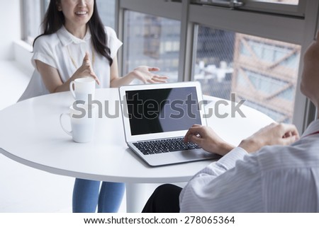 View of two young businesspeople talking at a table in office setting