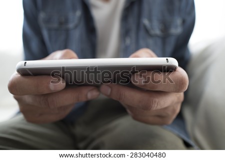 Closeup on a man\'s hands as he is sitting on a sofa and using a smart phone
