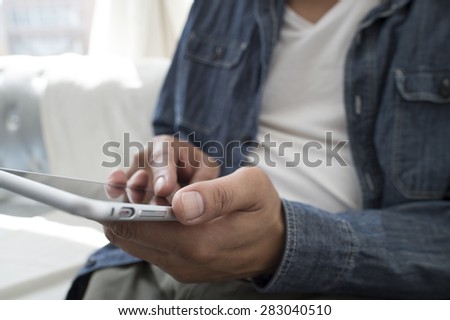 Side view of a casual smiling young man text messaging in sofa at home