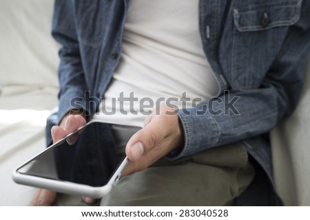 Close-up mid section of a well dressed man text messaging on sofa in living room at home