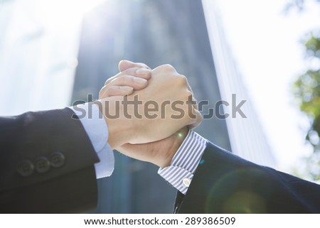 Business men and woman outside in front of tower building shaking hands