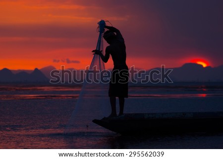 Silhouette of fisherman throwing fishing net during sunset