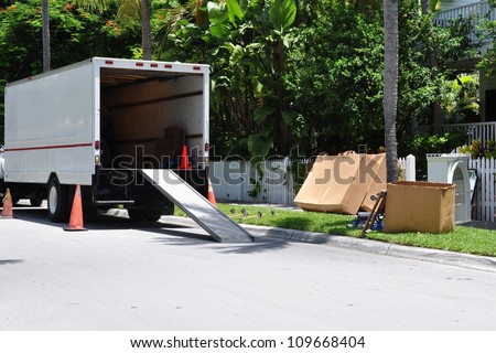 A Moving Van On Street With Ramp, Boxes And Household Furnishings
