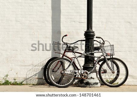 Two vintage bicycles locked to a lamp post against white painted brick wall.