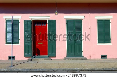 Typical New Orleans French Quarter Style Architecture With Green Shutters on a Pastel Pink Color Painted Stucco Wall and a Red Door with Mail Slot.