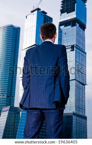 Businessman standing back against skyscraper in City