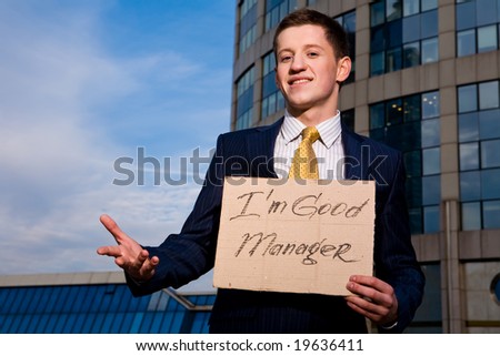 Financial crisis. Unemployment. Smiling young businessman holding sign I am good Manager outdoors