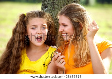 Funny mom and daughter listening music in headphones outdoors