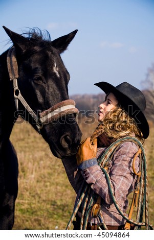 Lovely blond woman in a hat standing by horse in a field