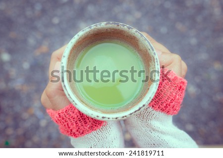 Two hands keeping warm, holding a hot cup of Japanese green tea in vintage mood