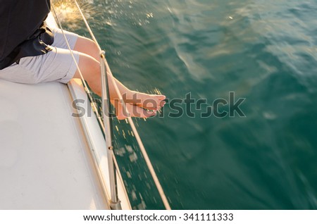 Man sit on yacht deck, legs outside of yacht under warm sunset flare