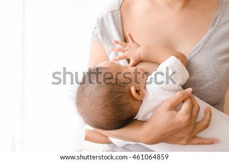 Mother breastfeeding her newborn baby beside window. Milk from mother\'s breast is a natural medicine to baby. Mother day bonding concept with newborn baby nursing.