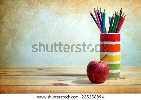 still life with apple and colored pencil on wooden table over grunge background