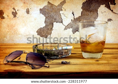 Still life with whiskey and cigarettes on wooden table over wall grunge background