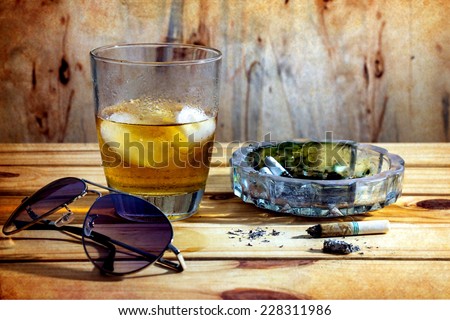 Still life with whiskey and cigarettes on wooden table over wall grunge background