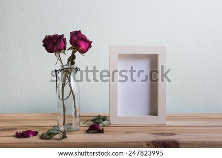 Still life with red rose and white photo frame on wooden table over grunge background, Valentine concept