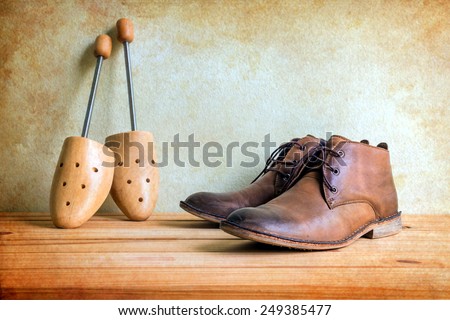 Still life with boots and wooden shoe tree on wooden table over grunge background