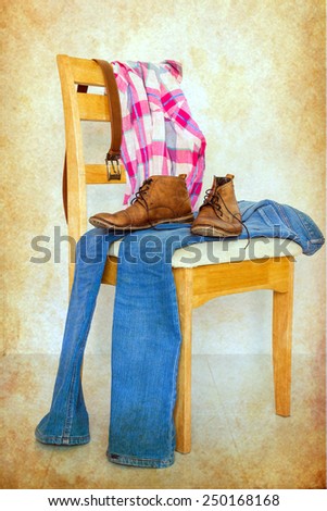 still life with plaid shirt, jeans and boots on wooden chair over grunge background