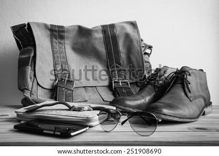 Still life with casual man, boots and bag on wooden table over grunge background, black and white