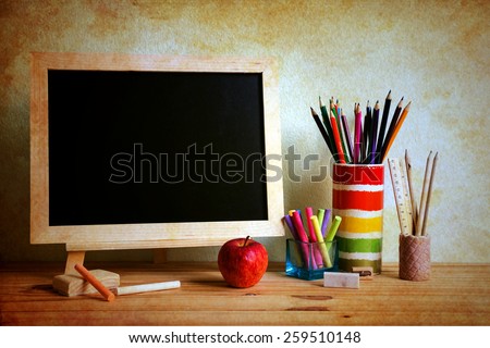 Still life with empty blackboard and colored chalks on wooden table over wall grunge background