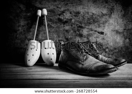 Still life with boots and wooden shoe tree on wooden table over grunge background, black and white