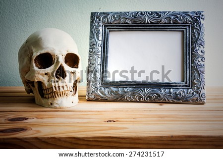 Still life with vintage photo frames and skull on wooden table over grunge background