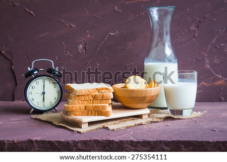 Milk with whole wheat bread and vintage black clock on brown stone table over stone grunge background.