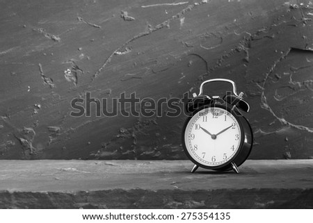 Still life with black vintage clock on stone table over stone grunge background, black and white