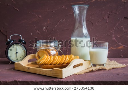 Milk with sandwich cracker and vintage black clock on brown stone table over stone grunge background.