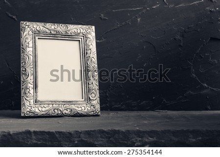 Still life with vintage photo frame on stone table over stone grunge background, black and white