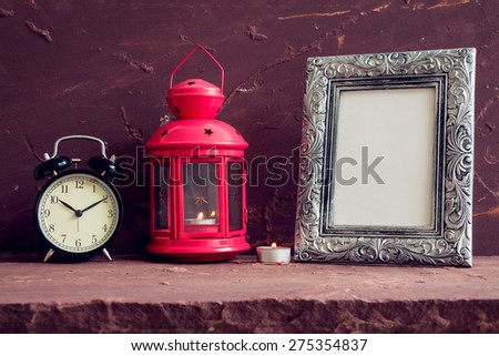Red lantern, candle, photo frame and black vintage clock on brown stone table over stone grunge background.