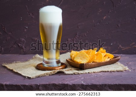 Potato chips on wooden plates and beer on brown stone table over stone grunge background.