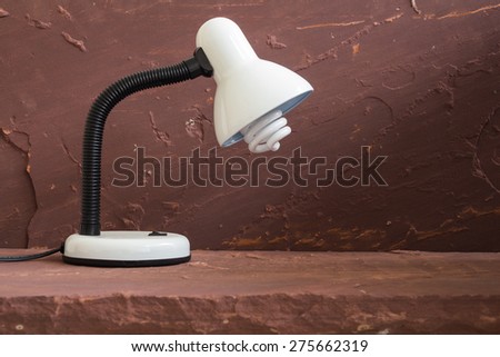 White desk lamp on brown stone table over stone grunge background.