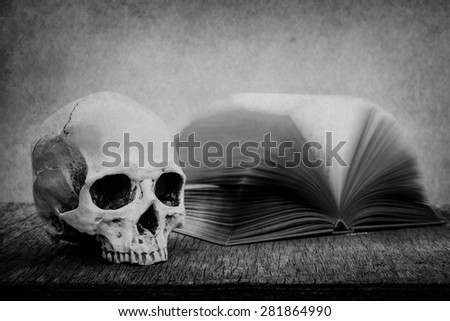 Still life with skull and old book on wooden table over grunge background, black and white