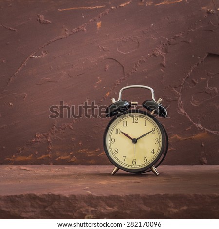 Still life with black vintage clock on brown stone table over stone grunge background