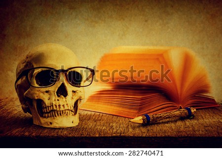 Still life with skull, old book and pencil on wooden table over grunge background