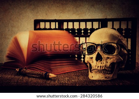 Still life with skull, old book,abacus and pencil on wooden table over grunge background