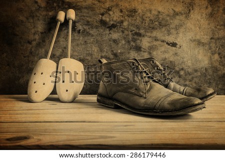 Still life with boots and wooden shoe tree on wooden table over grunge background, Black and white