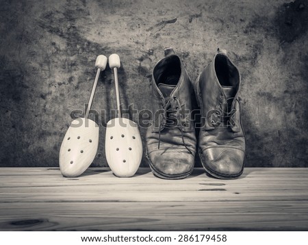 Still life with boots and wooden shoe tree on wooden table over grunge background, Black and white