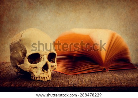 Still life with skull and old book on wooden table over grunge background