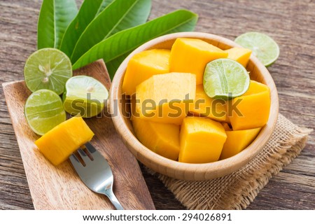 Slice of mango and green lemon in bowl on wooden background