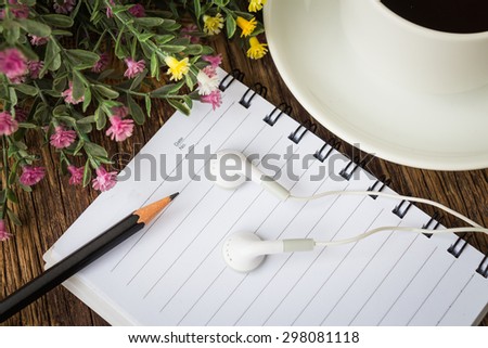 Notebook with pencil, white headphone and cup of coffee on wooden table background.