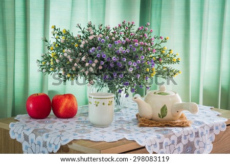 Bouquet of flowers with cup of tea and red apple on a wooden table over green curtain background in the bedroom