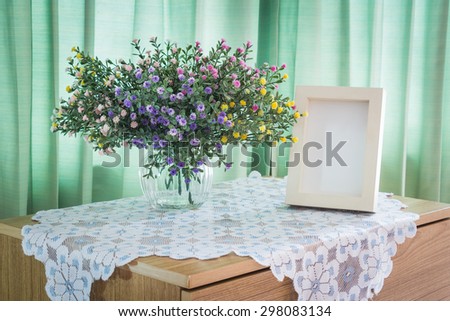 Bouquet of flowers and white vintage photo frame on a wooden table over green curtain background in the bedroom