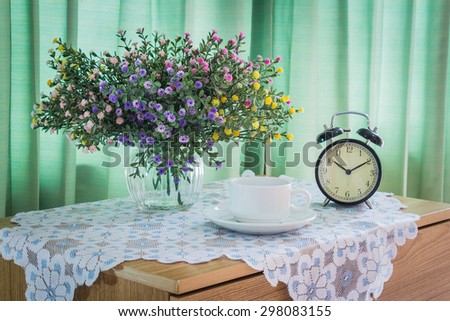 Bouquet of flowers with vintage clock and cup of coffee on a wooden table over green curtain background in the bedroom