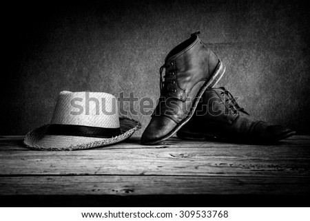 still life with boots and hat on wooden table over grunge background, black and white