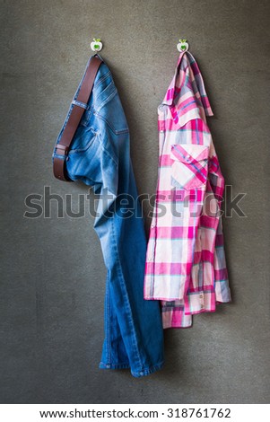 Men\'s casual outfits, blue jeans and pink plaid shirt hanging over gray grunge background