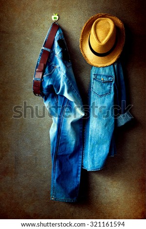 Men\'s casual outfits, blue jeans, jeans shirt and brown hat hanging over gray grunge background