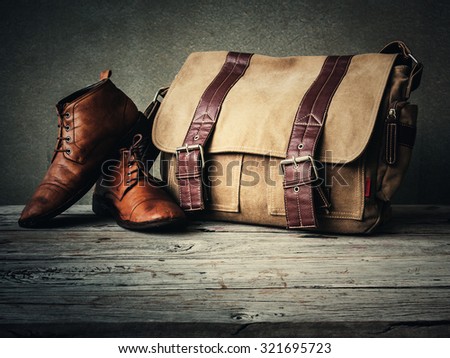 Men's boots and brown bag on wooden table over wall grunge background