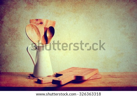 Kitchenware with wooden ladle, wooden spoon in white vase and wooden cutting boards on wooden table over grunge background